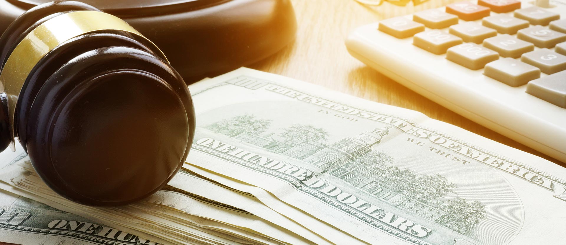 The image shows a gavel with a dollar bill on top resting on a keyboard next to a laptop, suggesting a theme of money, law, or justice.