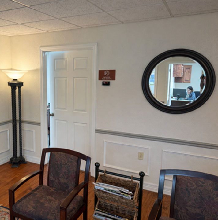 The image shows an interior space with a waiting area featuring chairs, a door, a circular mirror on the wall, and a sign indicating a no smoking policy.